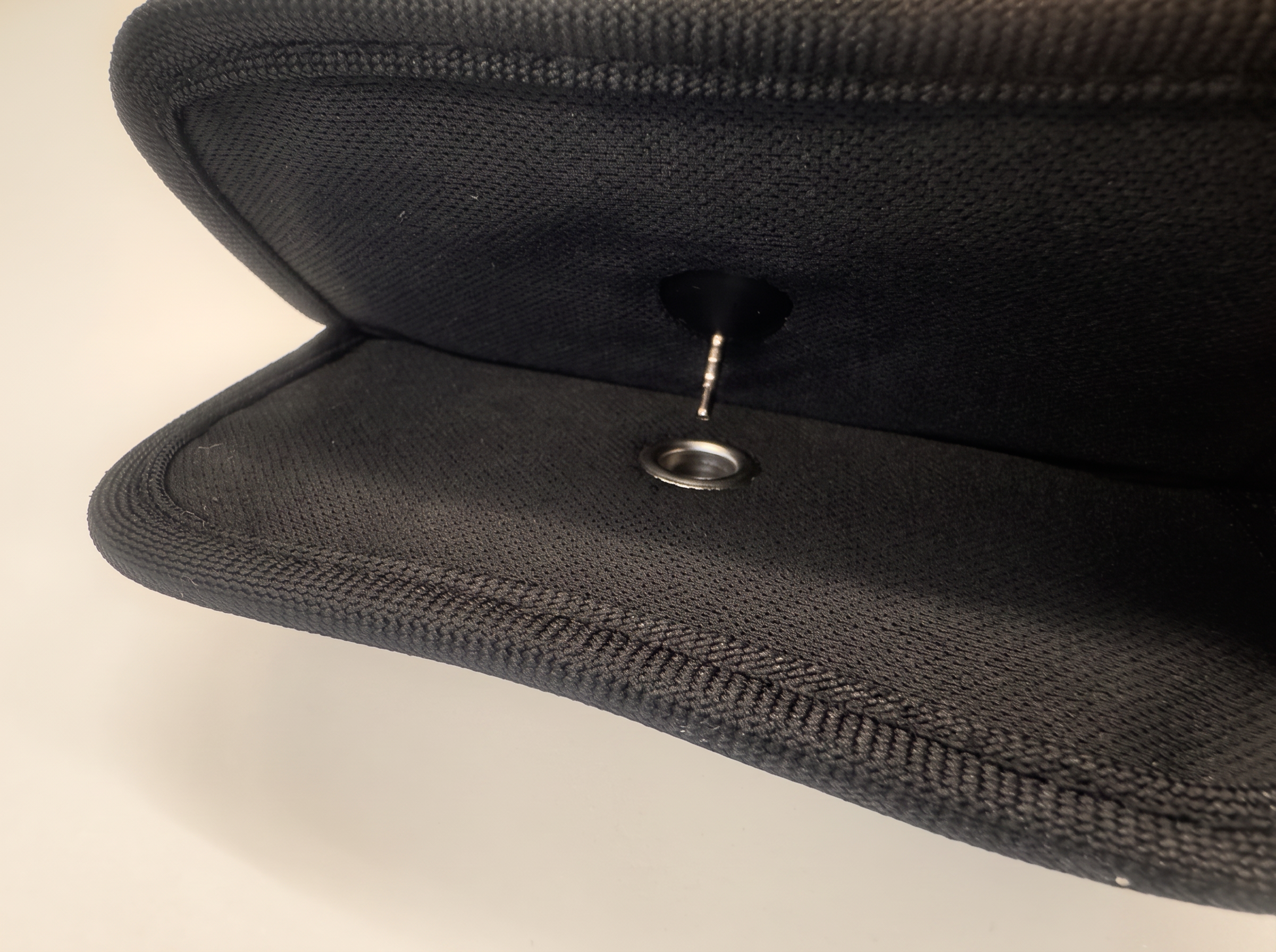 Macro close-up of the steel pin locking the pouch's neoprene opening.